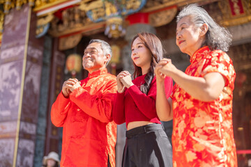 Asian family in red clothes making traditional Chinese New Year greeting gesture at temple, celebrating lunar new year with respect and joy, showing multigenerational and festive cultural appreciation
