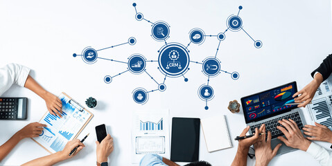 A diverse team collaborates over a white desk, utilizing data analysis tools and CRM graphics to enhance business strategies and communication across various sectors. Amity