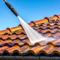 Close-up view of a high-pressure water sprayer cleaning a red tiled roof against a clear blue sky. Focus on the water stream