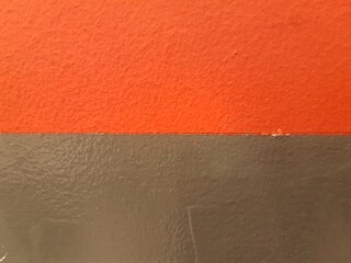 Abstract background of a wall painted half orange and half dark grey. Rough textured paint divided into two distinct contrasting color fields. Industrial or modern wall surface
