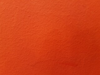 Full frame closeup of a vibrant orange painted textured wall surface. Abstract background of rough stucco or concrete painted a bright color. Detail of a bright reddish orange