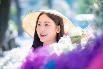 A young Vietnamese woman wearing a white ao dai and a conical hat stands beside a colorful street...