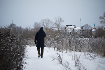 Solitary Winter Walk: Person in Blue Coat Walking on Snowy Path Towards Distant Buildings