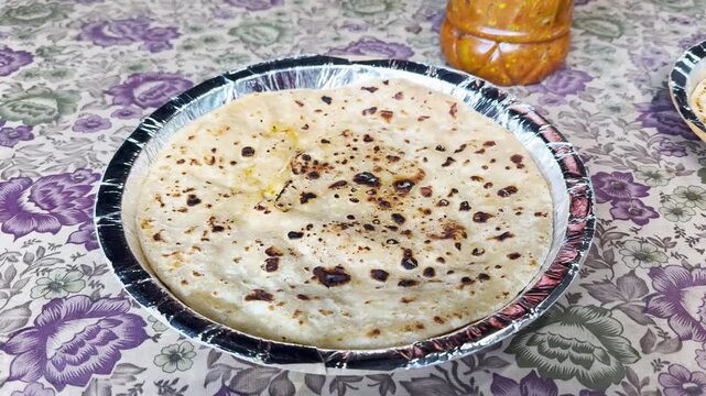 4K Closeup shot of Aloo Paratha served on a disposable paper plate besides the jar of pickle on a road side Dhaba for breakfast in Manali, Himachal Pradesh, India. Stuffed bread with spiced potatoes.
