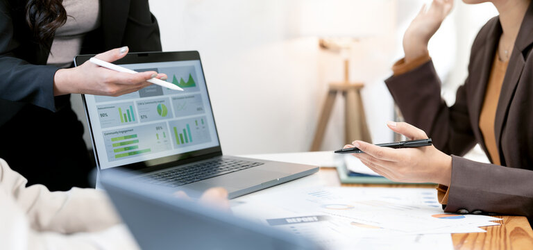 Close-up of business professionals analyzing financial charts and data displayed on a laptop screen during a focused and detailed corporate meeting.