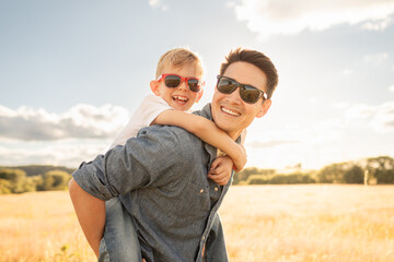 Happy Father Giving Son Piggyback in Sunny Field