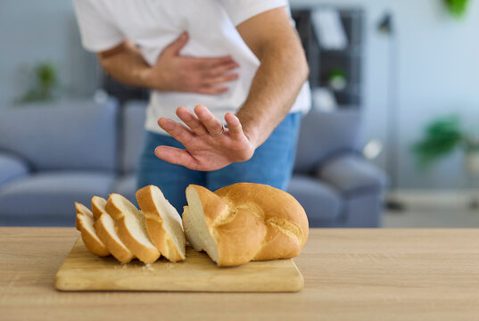 Gluten bread causes stomach pain and indigestion. A man rejects sliced loaf on board, showing celiac intolerance, risk of diarrhea and bloating. Clear dietary restriction and avoidance concept.