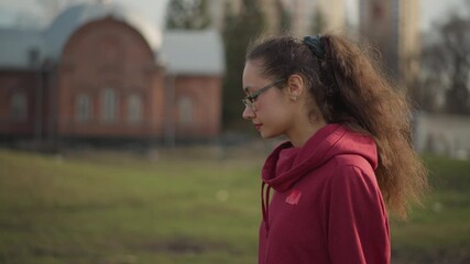 Girl In Open Field Turns Head Thoughtfully, Teenage Girl With Glasses Surveys Expansive Landscape Curiously, Young Girl With Tousled Hair And Glasses Examines Open Area With Wonder