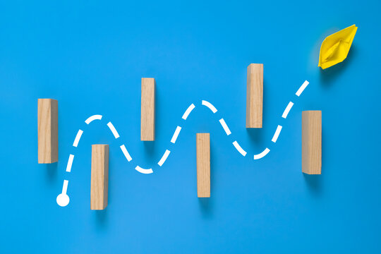 a yellow paper boat passes through barrier. isolated on blue background. concept of avoiding obstacle to achieve a goal