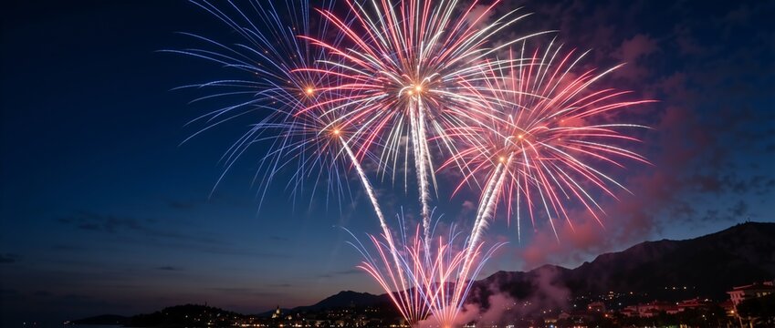 Red, white, and blue fireworks exploding in the night sky. Festive pyrotechnic display over a coastal town. Holiday celebration concept