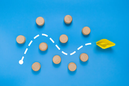 a yellow paper boat passes through barrier. isolated on blue background. concept of avoiding obstacle to achieve a goal