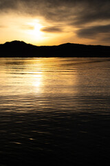 雲間から照らす太陽の光をさざ波の水面に反射する湖。