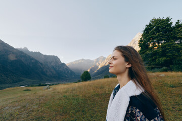 Obraz premium Woman profile portrait in mountains meadow, outdoors and contemplative with trees and distant peaks. Nature scene with calm expression, layered jacket and soft light over grassland.