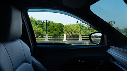 Interior on car close up on the seat and console inside of car. Can view landscape of side road with steel fence and forest under clear sky.