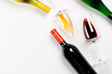 Wine glasses with red and white wine and bottles lying on white background