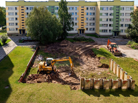 Excavators working on a residential courtyard construction site near apartment buildings, clearing soil and debris. Urban redevelopment and heavy machinery in action.