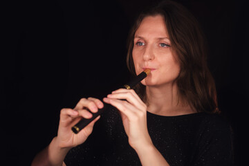 Fototapeta premium Woman playing a recorder or wooden flute whistle with focused expression on a dark background. Music performance or learning musical instrument concept.
