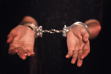 Woman hands in metal handcuffs on a dark background. Female with bound wrists. Concept of arrest,...