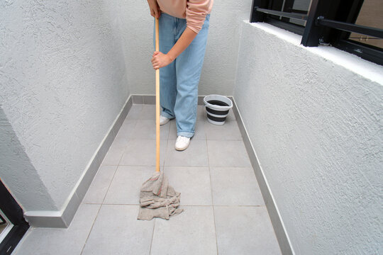 Woman mopping a tiled balcony floor with a bucket of water. House cleaning and domestic chore concept for hygiene and maintenance.