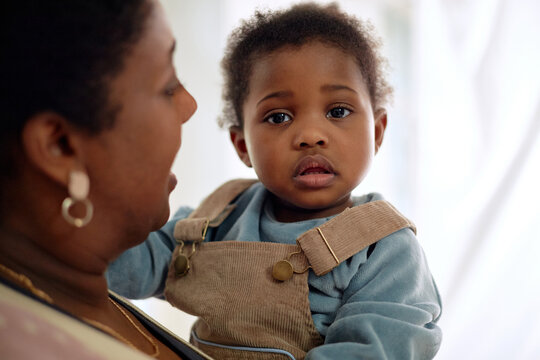 Portrait of Black woman holding Black toddler, toddler looking directly at camera with neutral expression, woman facing child, close up showing emotional connection