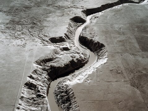 Aerial view of winding river cutting through rugged canyon terrain with dramatic erosion patterns and natural earthy textures