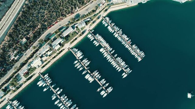 Aerial footage showcasing parallel docked yachts at Setur Marina, Kaş with clear blue waters, coastal infrastructure, and sunny lighting, capturing an inviting, serene marine atmosphere.
