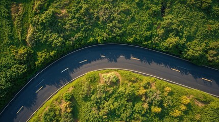 Serpentine asphalt road gracefully curves through a dense, verdant natural landscape from an aerial perspective.