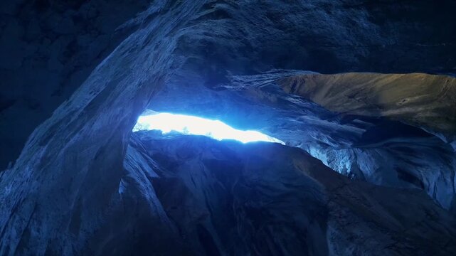 Dramatic view inside a frozen ice cave or crevice with a bright, luminous blue light shining through a narrow opening