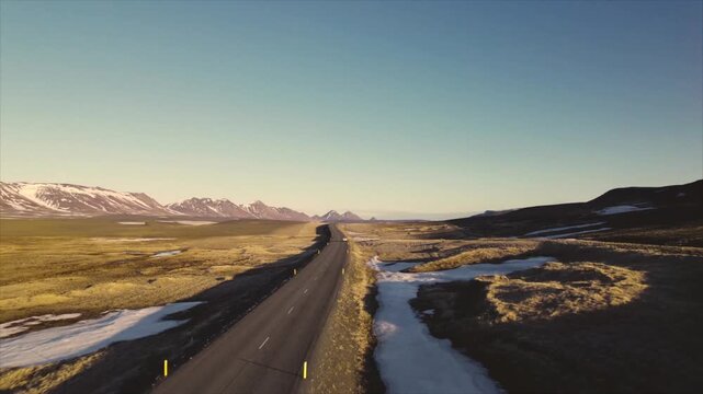 Empty Asphalt Road Through Vast Highlands with Snow Patches and Open Sky