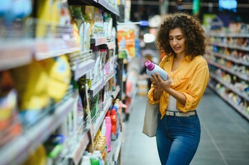 Woman comparing cleaning product label in supermarket aisle