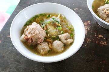 Delicious Indonesian meatball soup with noodles, broth, and herbs served in a white bowl.
