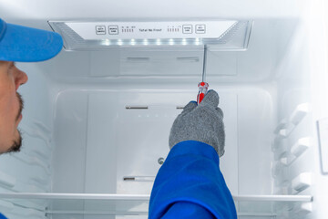 Repair worker fixes inside of refrigerator at home during day