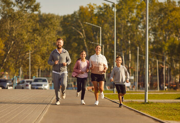 Family running in park, children jog together. Parents jog along a city park promenade, enjoying...