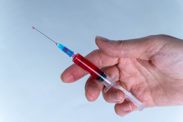 Hand holds a syringe filled with red liquid during a medical procedure in a clinic