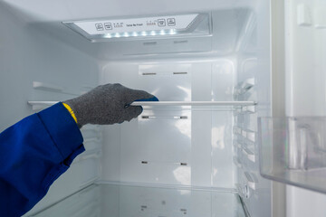 Hand removes a shelf from an empty refrigerator during cleaning process