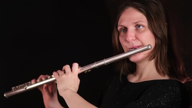 Woman playing the flute with a focused expression. Musician performing classical instrument. Music education and orchestral performance concept.