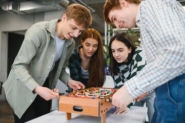 Cheerful young friends playing table football game in office