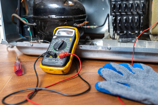 Repair technician checks electrical connections inside refrigerator on a workbench