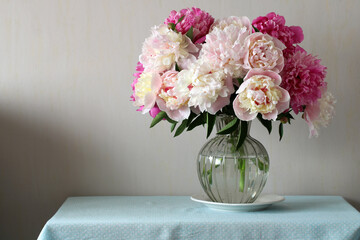 Peonies bouquet in glass vase on blue tablecloth