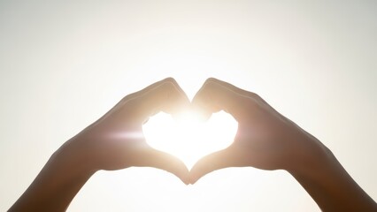 Fototapeta premium Hands forming a heart shape against the bright sun, symbolizing love, hope, and connection in a warm, glowing light