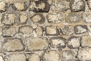 Masonry of a wall made of grey round and oval stones bonded with cement and lime mortar