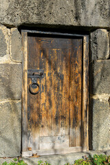 A weathered wooden door in the wall of a church made of large stone blocks. An iron bolt and a ring-shaped knocker. Gohnari, Javakheti region of Georgia.