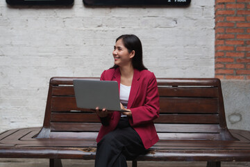 Young businesswoman smiling using laptop on bench