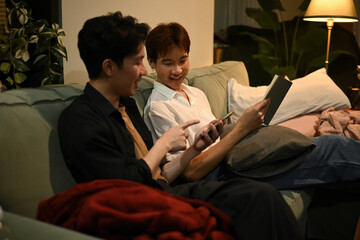 Partners unwind together, one reading and the other sharing a funny moment on his phone, creating a warm and intimate home atmosphere