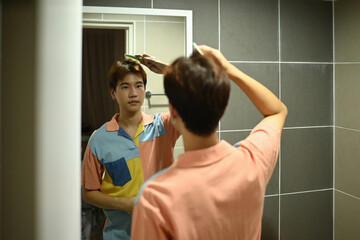 A morning grooming routine as a young man styles his hair in front of a mirror, wearing a colorful casual shirt