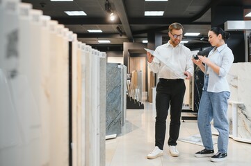 Shop assistant showing ceramic tile to woman in hardware store