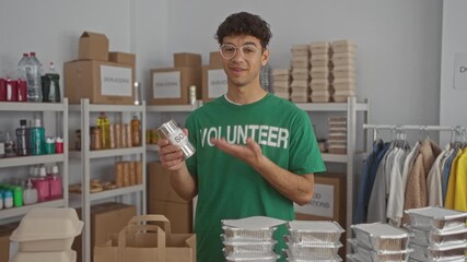 Man in green volunteer shirt holding soup can with hand inside a donation center building; compassion service. - Powered by Adobe