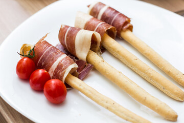 Grissini breadsticks wrapped in prosciutto and served with tomatoes