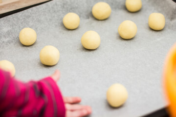 Balls of dough on baking sheet with child's hand reaching out