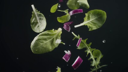 Fresh green salad ingredients with vibrant purple onion pieces falling in slow motion against a dark